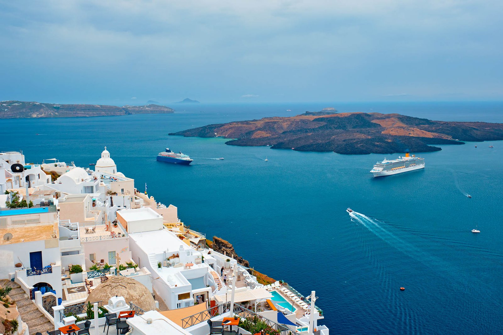 View of Fira Greek town with traditional white houses on Santorini island with cruise ships in sea. Santorini, Greece